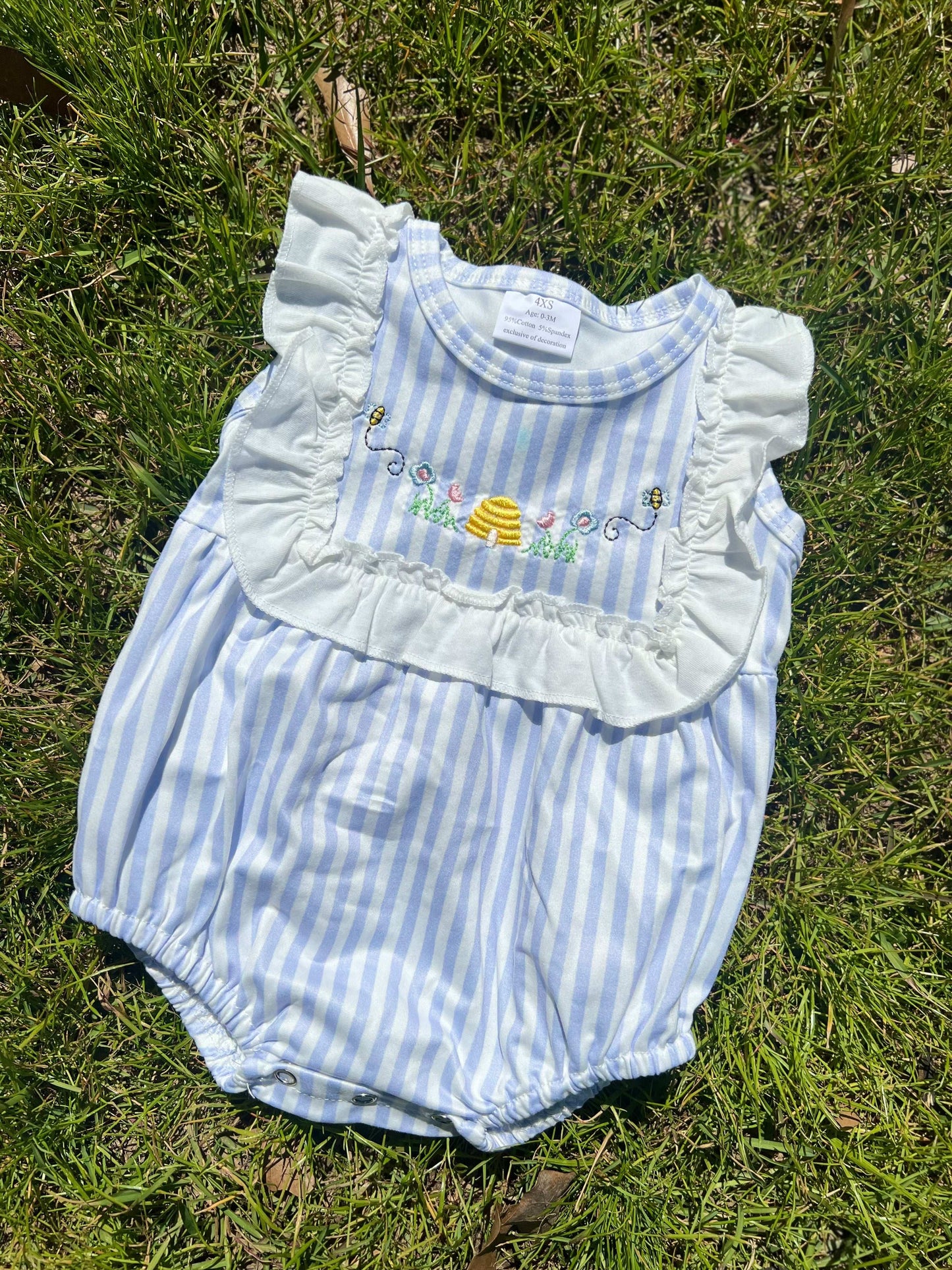 Child's bubble romper with blue stripe pattern and ruffled chest. Embroidered design with beehive, flowers, and bees.